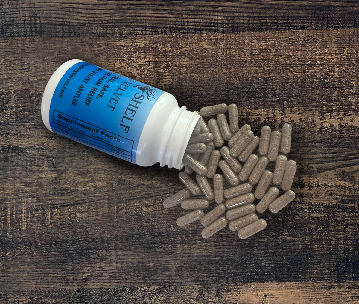 A white supplement bottle with a blue label lies on its side on a dark wooden surface, with brown capsules spilling out onto the wood.